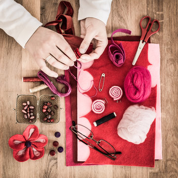 Hands of hobbyist making felt flowers - felting supplies on wooden table - high angle, square. 