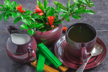 A small cup of coffee, a jug of milk, chocolate and pomegranate tree branches with flowers on a dark background