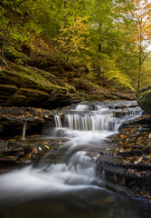 A tiered waterfall with in a forest with fall colors.