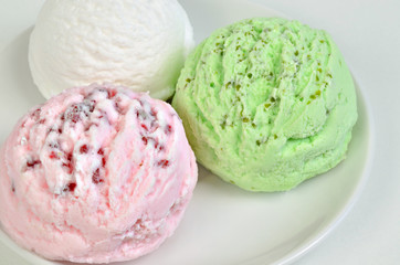 Erdbeereis, Vaniileeis und Pastazieneis / drei eiskugeln, weiß, pink und grün auf einem Teller, Makro, horizontal 