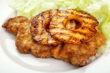 Fried schnitzel ( tenderized and breaded pork fillet cutlet ) with grilled pineapple slices and lettuce in background - 109882555