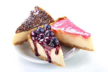Three cheesecake slices , chocolate , pink sugar frosting and jam with fresh blueberries , white background