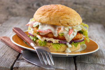 Salmon and shrimp burger , mayonnaise on bottom bun , breaded salmon shrimp patty and tartar sauce...