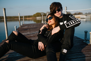 Young happy couple in sunglasses resting on a pier and embracing on a sunny summer day. Love concept