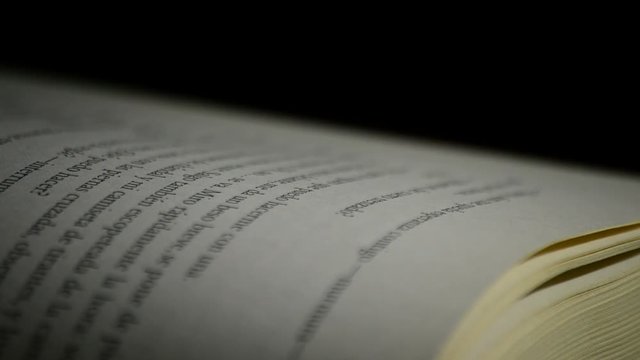 Detail of pages, texts, words and phrases of open book in castillian gyrating at black background