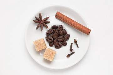 White saucer with coffee beans, spices and cane sugar against white background, top view with place for text