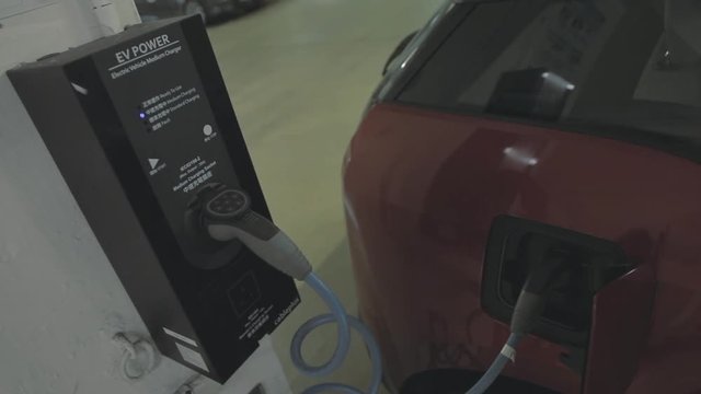 Sedan car getting recharged at a new electric vehicle charging station in Hong Kong. Alternative energy. Close  up handheld shot.
