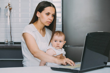 a young mother with a child in the kitchen sitting at the laptop