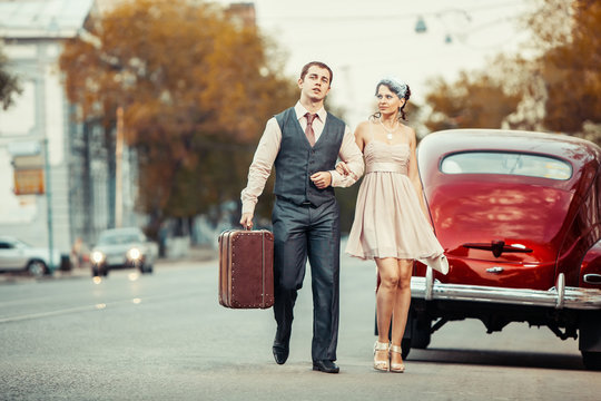 Pretty walking couple with the suitcase on the vintage car backg