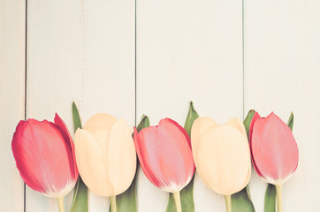 Background with tulips and wooden planks. Yellow and pink tulips on a wooden background (vintage)