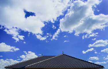 Modernes Ziegeldach als Zeltdach mit dunklen Tonziegeln und Pinienzapfen als Dachschmuck vor sommerlichem Himmel