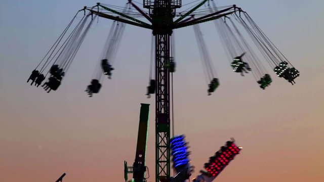 Fairground attractions by rotating at sunset with large colorful of neon lights and motion. (06)