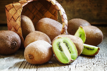 Kiwifruit poured out of a wicker basket, vintage wooden backgrou