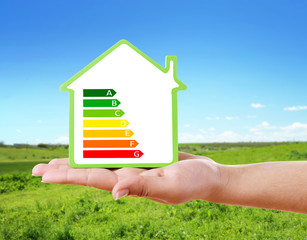 Naklejka premium Female hand holding house with energy efficiency scale image on natural background