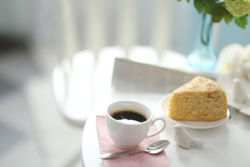 Cup of coffee with cake on white table in light interior
