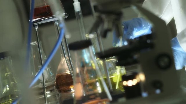 A water like substance is poured from a graded cylinder into a glass chemistry beaker containing a clear liquid. Close up  gel lighting
