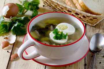 Soup of young nettle with meat and egg on a wooden background.