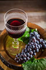Tasty wine in glass with grapes on wooden barrel