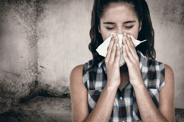 Composite image of beautiful woman sneezing in a tissue