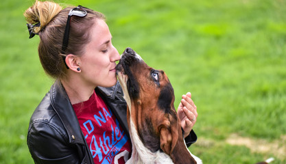 Young woman with an affectionate one year old Basset hound (Canis lupus familiaris) in the yard of a hobby farm.  Girl loves her dog, wet kisses from her one year old Basset hound .