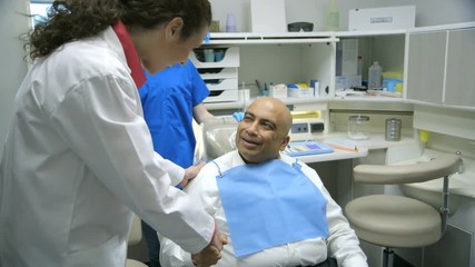 A female dentist greets her patient who is waiting in the dental chair.