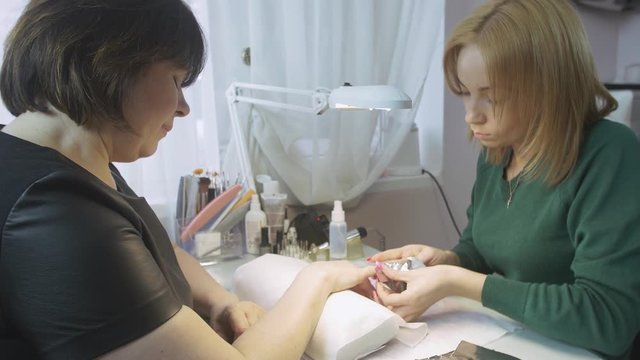 Manicurist put cotton pad and foil on nail to adult woman in beauty saloon. Removal of shellac cover. Medium shot