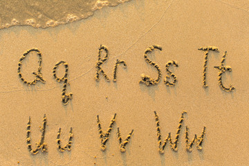 Alphabet written by hand on sandy beach (letters from Q to W)