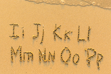 Alphabet written by hand on sandy beach (letters from I to P)