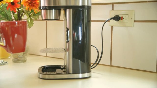 An environmentally minded woman conserves energy by unplugging the coffee maker after the coffee is ready.