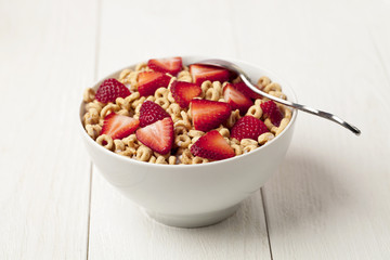 bowl of ring cereals with strawberry and a spoon