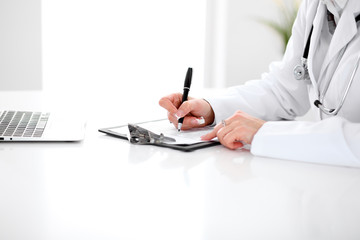 Close-up of a female doctor filling  out application form , sitting at the table in the hospital