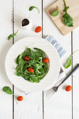 Rocket salad with cherry tomatoes on white wooden background