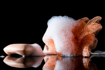 Orange sponge body with foam near soap with reflection isolated on black background