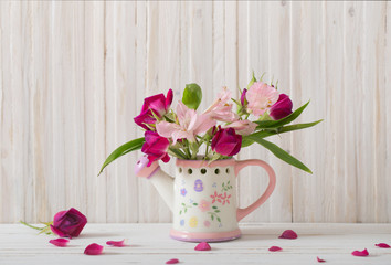 bouquet of bright flowers in watering can on wooden background