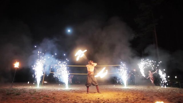 Fire show performance. Male fire performer twirling fire baton. Female fire performers dance spinning sparkling fireworks poi