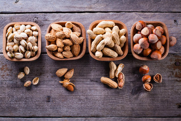 Hazelnuts, pistachios, peanuts and almonds on wooden bowls.