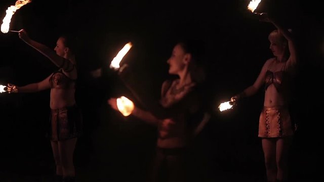 Fire show performance. Group of hot women &ndash; female fire performers dance gathering up burning fire torches on black background. Slow motion
