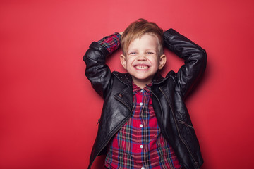 Fashion little boy wearing a leather jacket. Studio portrait over red background
