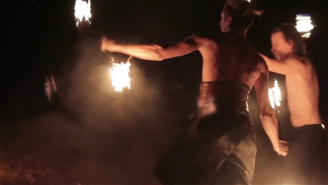 Fire show performance. Three handsome male fire performers dance twirling two fire batons staff ignited from both sides each. Slow motion

