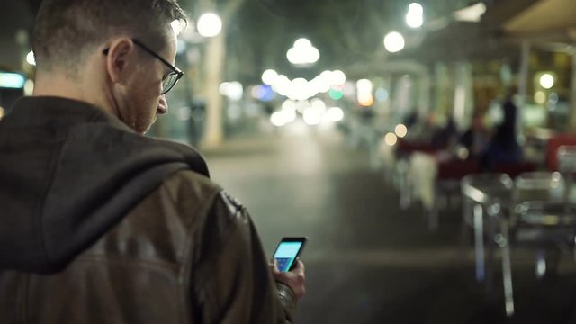 Man walking on the street at night and texting on smartphone, steadycam shot
