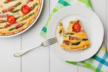 Tart with asparagus and tomatoes on white wooden background.
