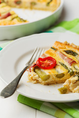 Tart with asparagus and tomatoes on white wooden background.