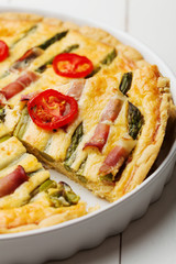 Tart with asparagus and tomatoes on white wooden background.