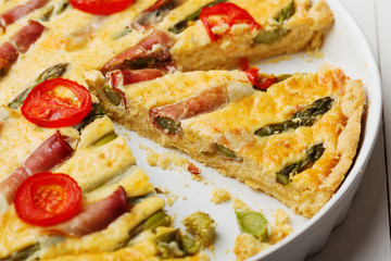 Tart with asparagus and tomatoes on white wooden background.