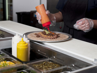 mid section of a chef putting sauce while making burrito.