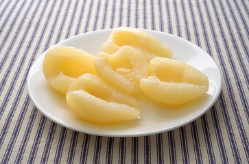 Pears halves on a white plate atop a striped tablecloth side view