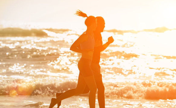 Fitness couple running along the beach during sunset