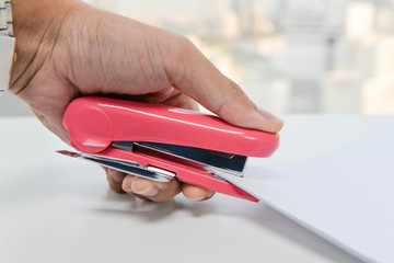 Human hand is stapling the paper with pink stapler