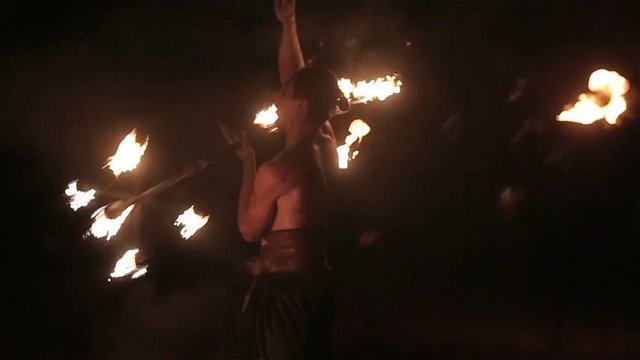 Fire show performance. Handsome male fire performer twirling fire baton with several wicks - dragon staff. Close-up. Slow motion