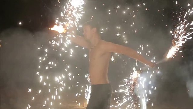 Fire show performance. Male fire performer dance twirling sparkling fireworks batons staff. Slow motion